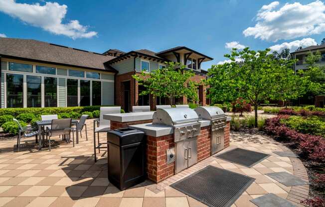 One BR Apartments in Greenville SC - Velo Verdae - Outdoor Grill Station with Brick and Stainless Steel Grill Sets, Counter with Bar Chairs, Table Seating, and Surrounding Trees