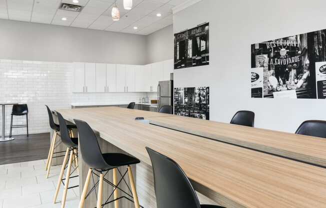 a communal table with black chairs in a room with a kitchen