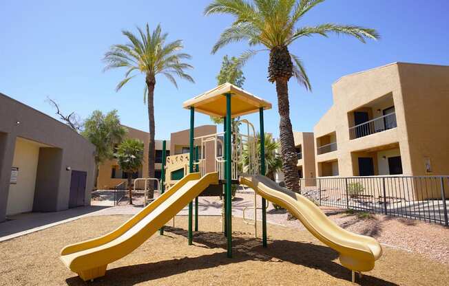 A playground with a yellow slide and palm trees.