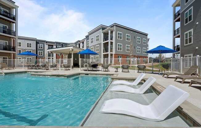 A pool area with white lounge chairs and a blue umbrella.