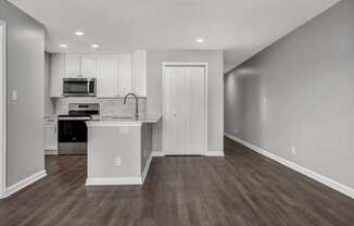 an empty living room and kitchen with white cabinets and a counter top