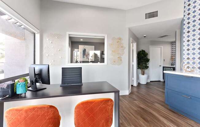 A modern office with a black desk and orange chairs.