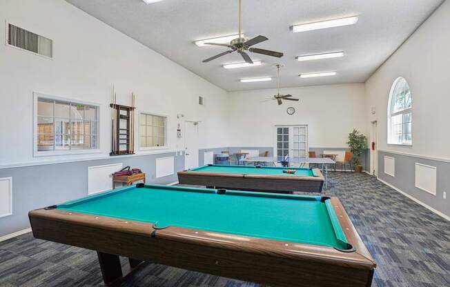 A pool table in a room with a ceiling fan and lighting.
