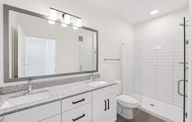 A bathroom with a sink, mirror, toilet and shower.