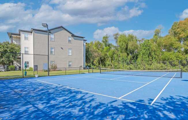 A blue tennis court is surrounded by apartment buildings at Ultris Island Park in Shreveport, LA