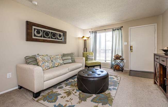 A living room with a beige couch, a round ottoman, and a floral rug.