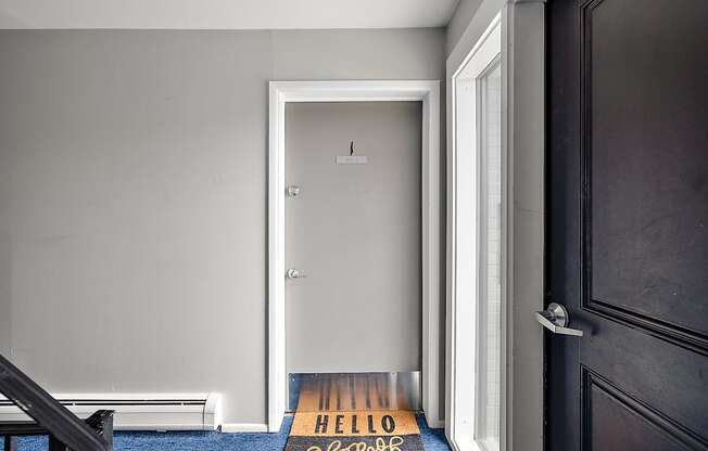 A black door with a mat that says "HELLO" on it.