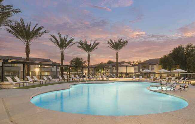 a swimming pool with chairs and palm trees at dusk