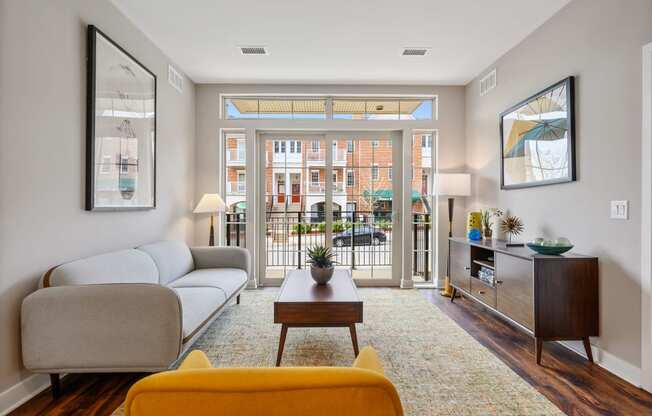 A living room with hardwood-style flooring, double doors to a private balcony, and ample natural light.