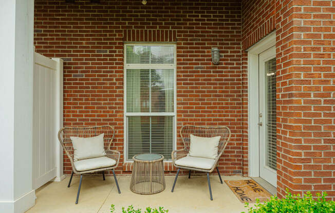 a patio with two chairs and a table in front of a brick house