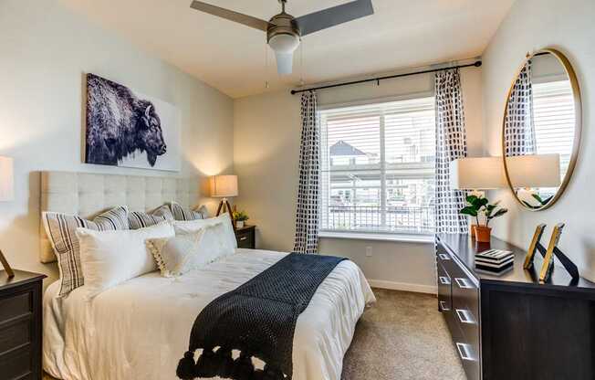 A bedroom with a large bed, a painting of a bison, and a ceiling fan.