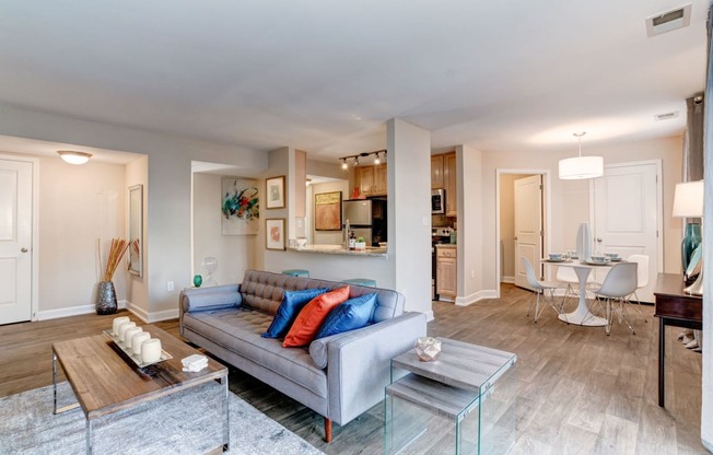 a living room with a couch table and chairs and a kitchen in the background