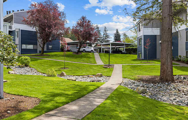 A pathway leads through a grassy area with a tree and a building in the background.