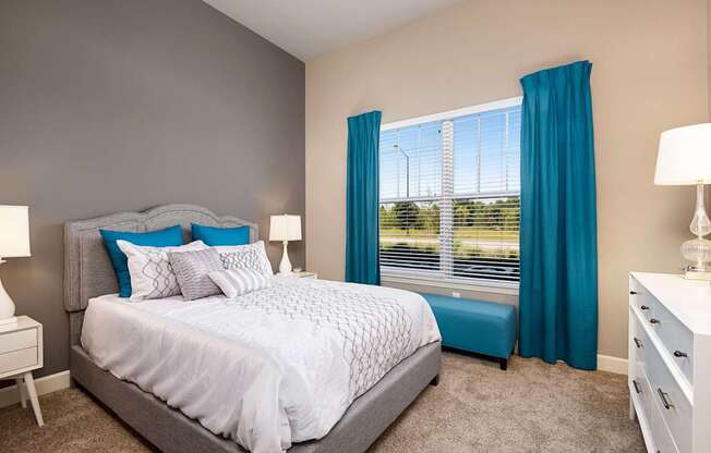 A bedroom with a large bed and a window with blue curtains.