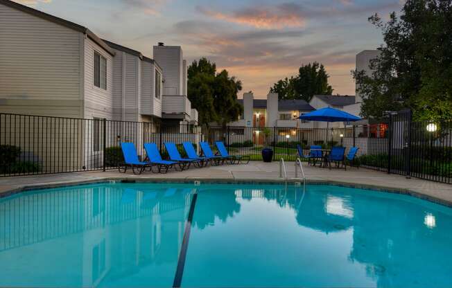 Swimming Pool Lounge Area at dusk with bright blue chairs and umbrellas at Cobblestone Creek Apartments, Roseville