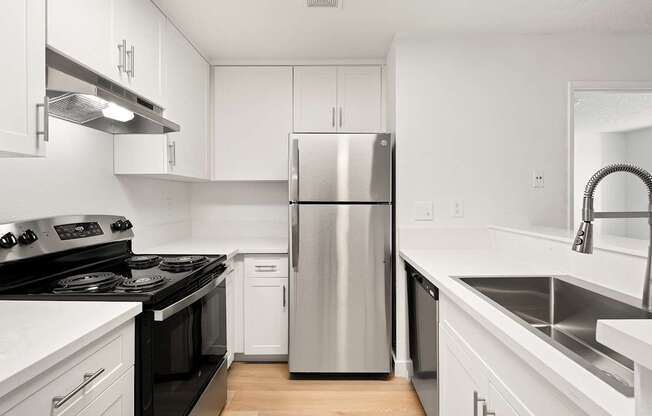 A modern kitchen with a stainless steel refrigerator and black countertops.