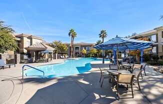 A swimming pool with a blue umbrella and chairs around it.