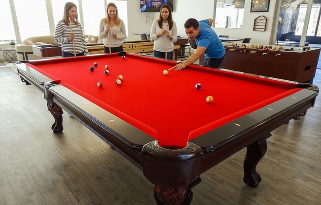 A man is about to take a shot at a pool table with three women watching.