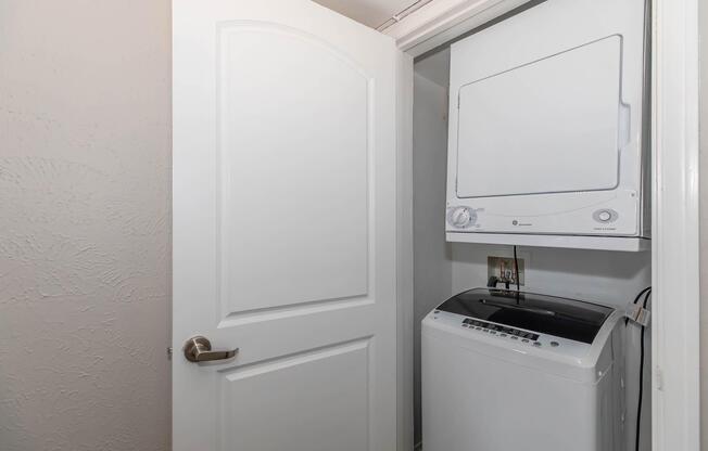 A small laundry room featuring a stacked washer and dryer unit. The door is ajar, revealing the appliances which are white and modern. The walls are painted a light color, providing a clean and functional space for laundry chores.