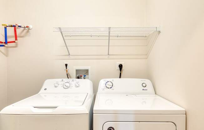 two washers and a dryer in a laundry room with a shelf above them