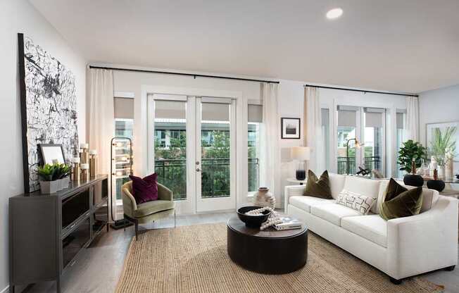 A modern living room with a white sofa, a coffee table, and a large window with curtains.