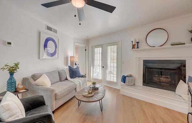 A living room with a grey couch, a coffee table, a fireplace, and a ceiling fan.
