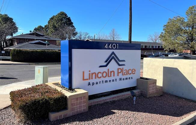 A blue and white sign for Lincoln Place Apartment Homes sits in front of a building.