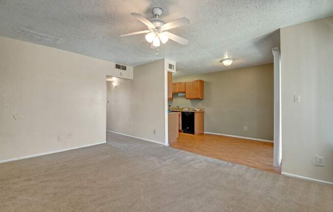 an empty living room with a ceiling fan and a kitchen
