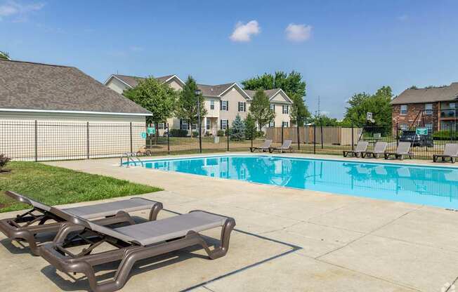 A pool with a sun lounger in front of a fence and houses in the background.