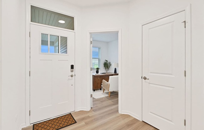 A white door with a glass window is open to a room with a desk and a chair.
