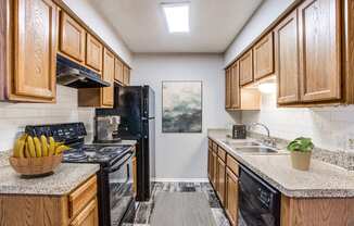 Apartments for Rent in Fort Worth- Monarch Pass- Kitchen with Black Appliances, Wooden Cabinets, and Tile Backsplash