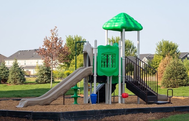 A playground with a green slide and a green umbrella.