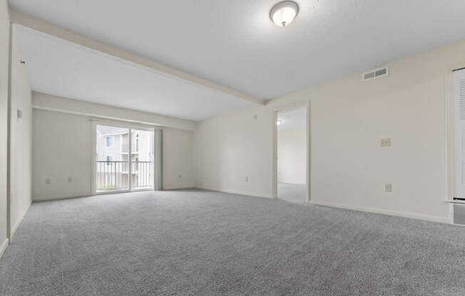 A spacious living room with a carpeted floor and a sliding glass door to a balcony at Fieldstream Apartment Homes in IA 50023