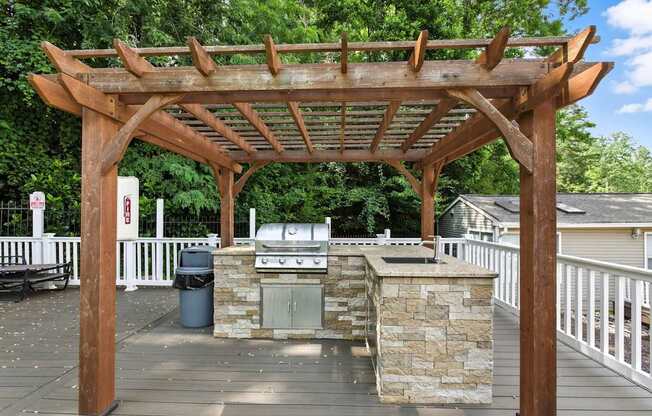 A wooden pergola with a stone base is situated on a wooden deck.