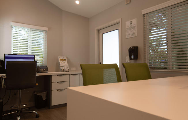 A white desk with a computer and two chairs in front of a window.