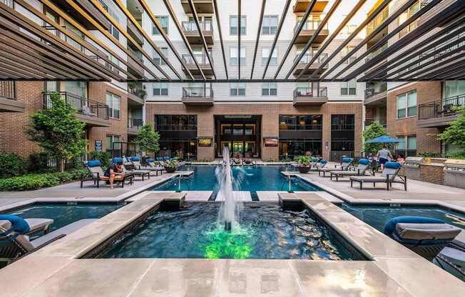 A large fountain in the middle of a pool surrounded by lounge chairs.