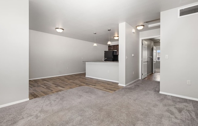 A spacious living room with a grey carpet and white walls.
