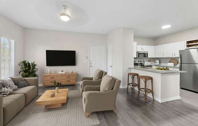 A modern living room with a grey sofa, a wooden coffee table, and a kitchen area in the background.