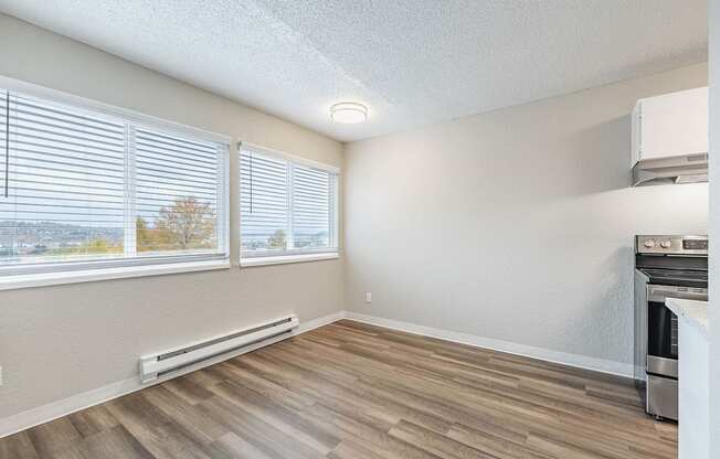 Bright kitchen and dining area with a stove, window blinds, and wood-style flooring in a Peak 88 Apartment home in Renton, WA.