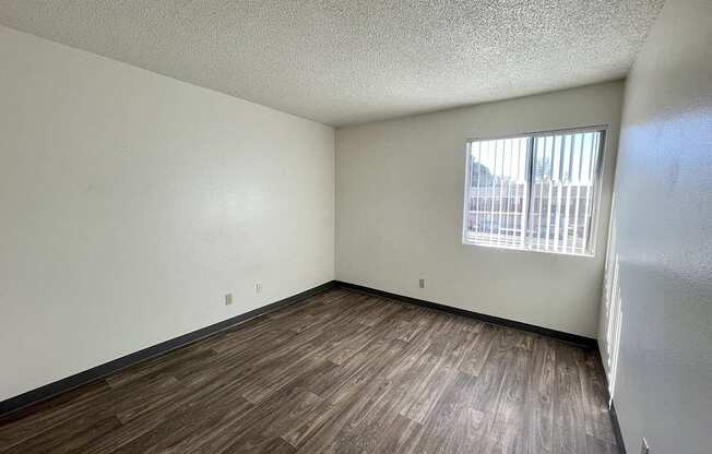 A room with wooden flooring and a window with blinds.