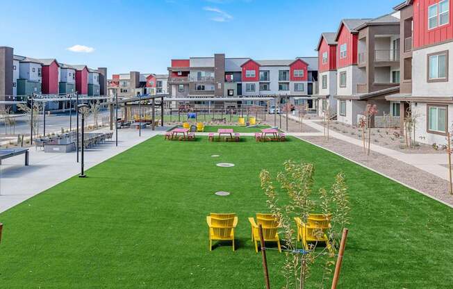 A grassy area with yellow chairs and a playground in the background.