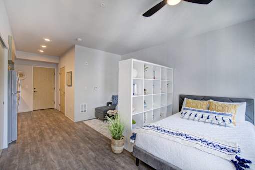 A bedroom with a bed, a plant, and a fan.