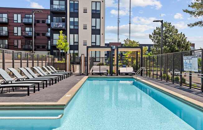 A large swimming pool in front of a building with lounge chairs around it.
