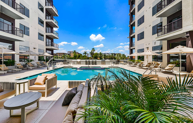 A pool surrounded by chairs and plants with apartment buildings in the background.
