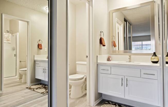 Single vanity area with white quartz counter tops, white cabinet, mirrored closet door and bathroom on the left