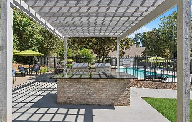 Outdoor BBQ Area with Canopy and View of Swimming Pool at Retreat at Stonecrest Apartments located in Lithonia, GA.