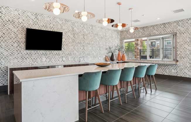 a kitchen with a long bar with blue chairs and a television