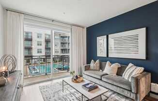 A modern living room with a grey sofa and a large window overlooking a pool.