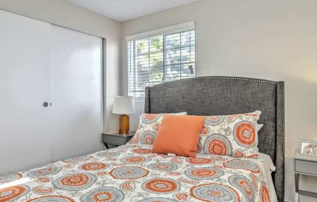 A bed with a grey headboard and orange and blue bedspread with matching pillows.