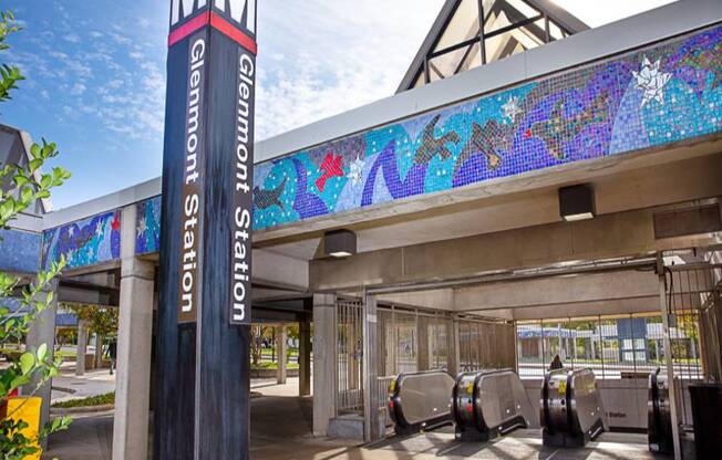 A tall pillar with the letters MM on it stands in front of a building with a mosaic on the roof.